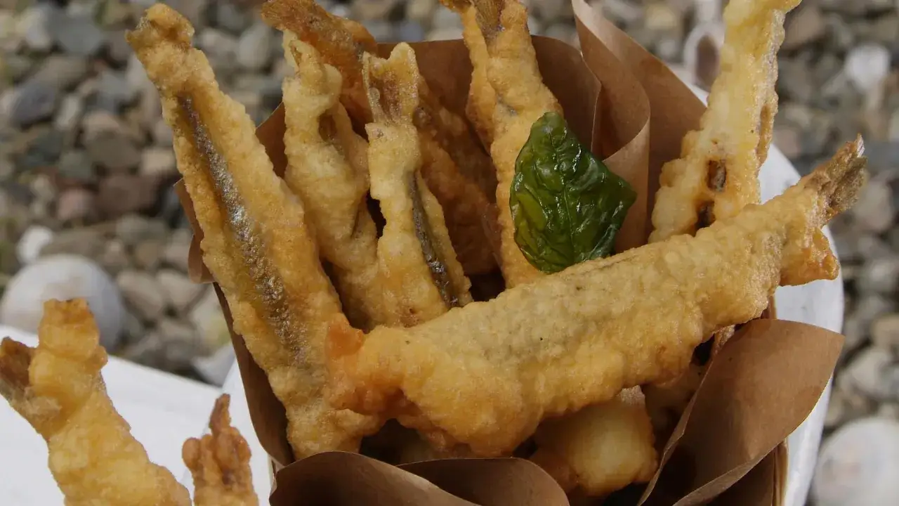 Accras de poisson croustillants, dor&eacute;s et app&eacute;tissants, servis dans un cornet en papier brun. Une feuille de basilic apporte une touche de fra&icirc;cheur.