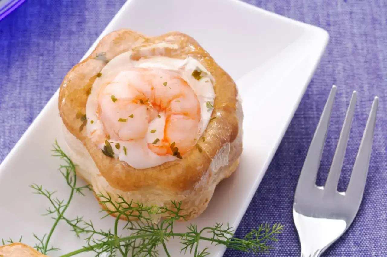 Un d&eacute;licieux vol au vent crevettes, garni d'une sauce cr&eacute;meuse et d'une crevette rose, sur une assiette blanche avec une touche d'aneth.