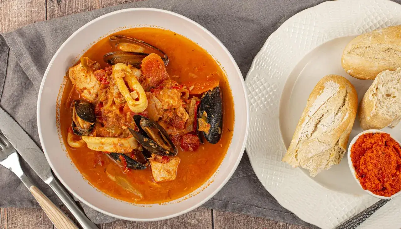 Un plat de bouillabaisse riche en fruits de mer, avec des moules, du poisson et des calamars dans un bouillon orang&eacute;. Accompagn&eacute; de pain et de rouille, parfait pour une recette de bouillabaisse authentique.