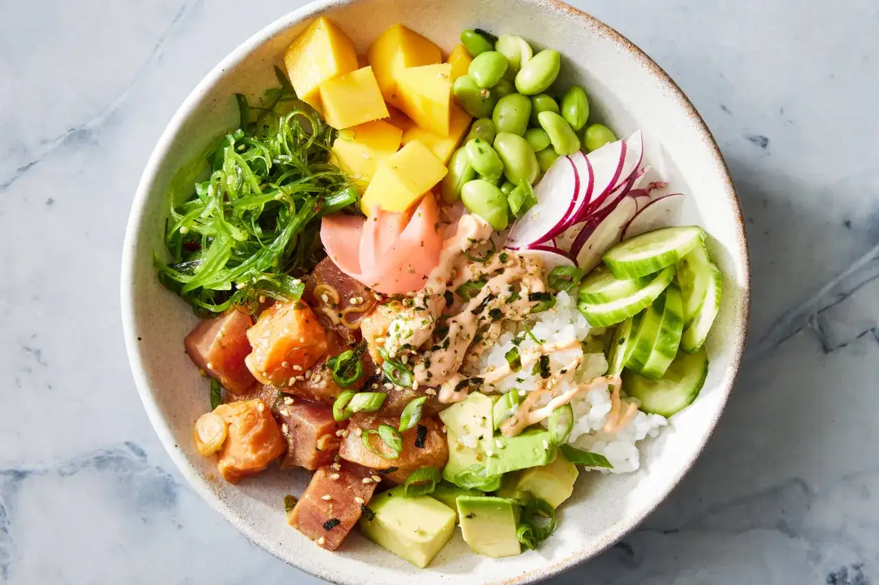Un délicieux poke bowl coloré avec du thon, de la mangue, de l'avocat, des edamames, des radis, du concombre et des algues.