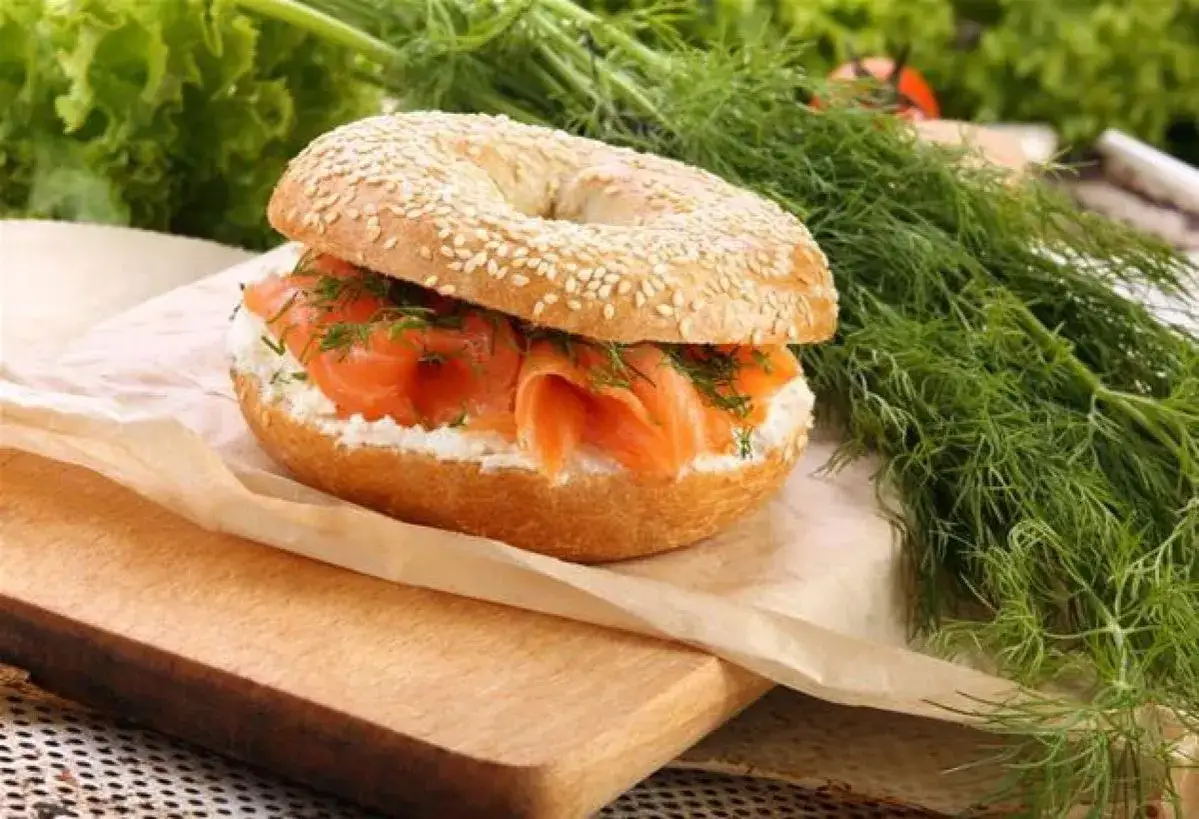 Un bagel saumon garni de fromage frais et d'aneth, prêt à être dégusté.