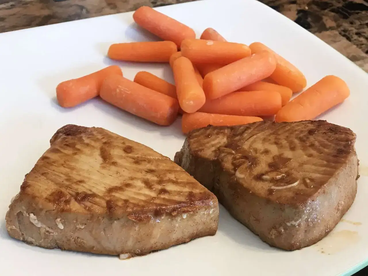 Deux steaks de thon frais po&ecirc;l&eacute;s, accompagn&eacute;s de carottes miniatures. Une id&eacute;e simple pour une recette thon frais savoureuse.