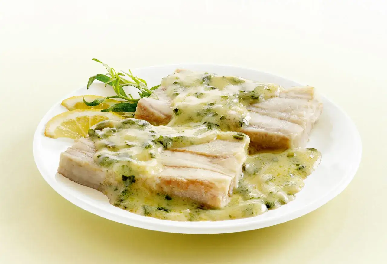Deux pav&eacute;s de poisson napp&eacute;s d'une onctueuse sauce &agrave; l'oseille, accompagn&eacute;s de quartiers de citron et d'une herbe fra&icirc;che.