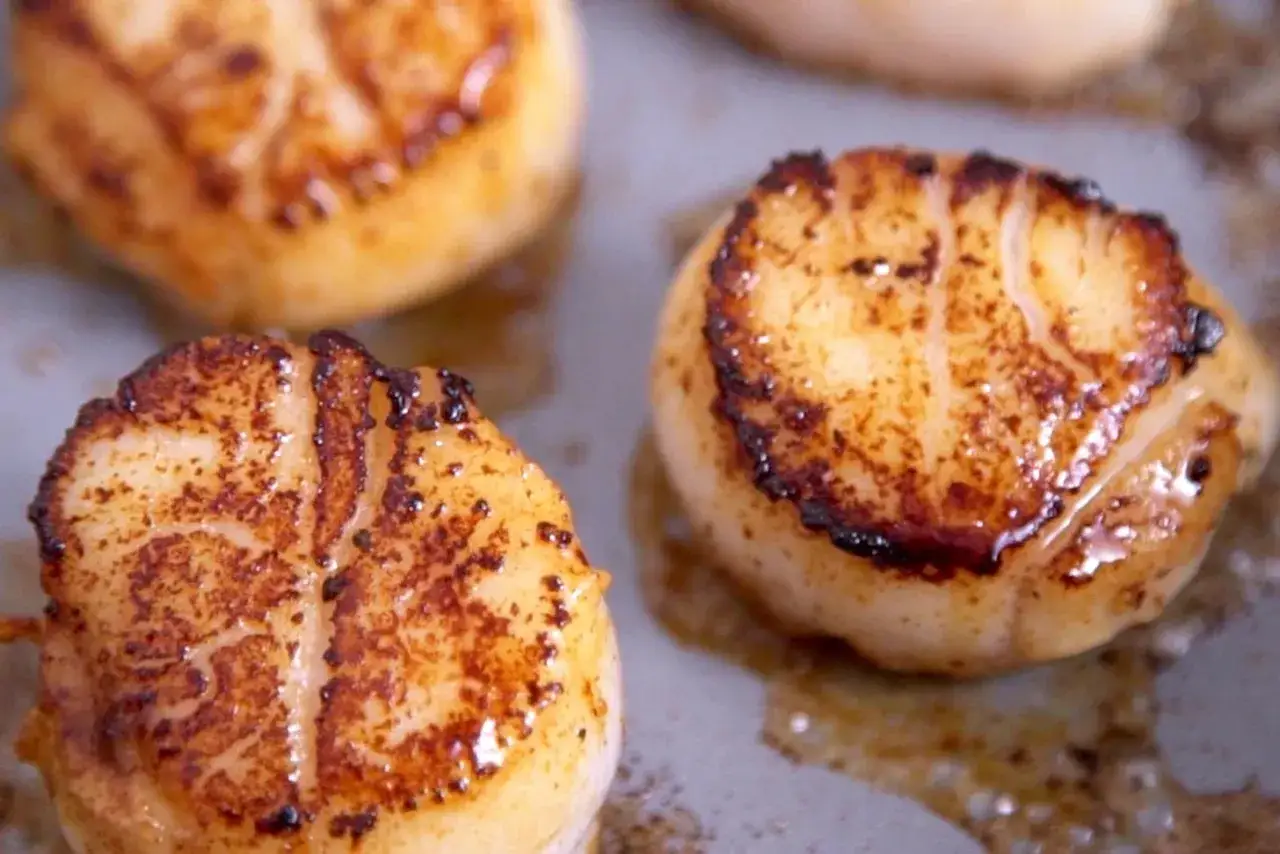 Trois noix de petoncle dorées et caramélisées, prêtes à être dégustées.