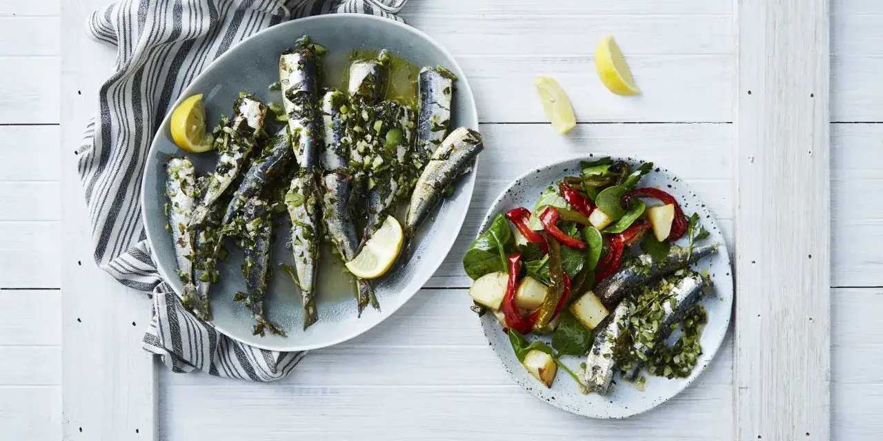 Deux assiettes de sardines grill&eacute;es, l'une avec une salade de poivrons et pommes de terre, l'autre nature, garnies de citron et d'herbes. Un accompagnement sardines grill&eacute;es parfait.