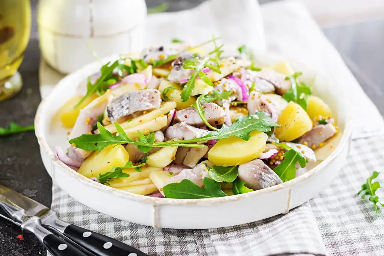 Salade de pommes de terre et de hareng, garnie de roquette et d'oignons rouges.