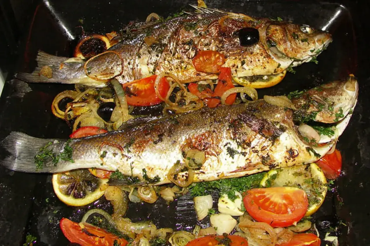 Deux poissons entiers r&ocirc;tis avec des rondelles de citron, des tomates, des oignons et des olives. Un plat savoureux de bar poisson.