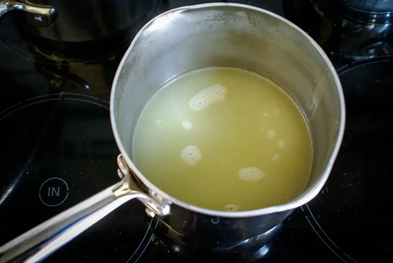 Une casserole en m&eacute;tal contient un liquide jaune p&acirc;le, signe d'un fumet de poisson en pr&eacute;paration. Des bulles remontent &agrave; la surface, promettant une saveur riche.