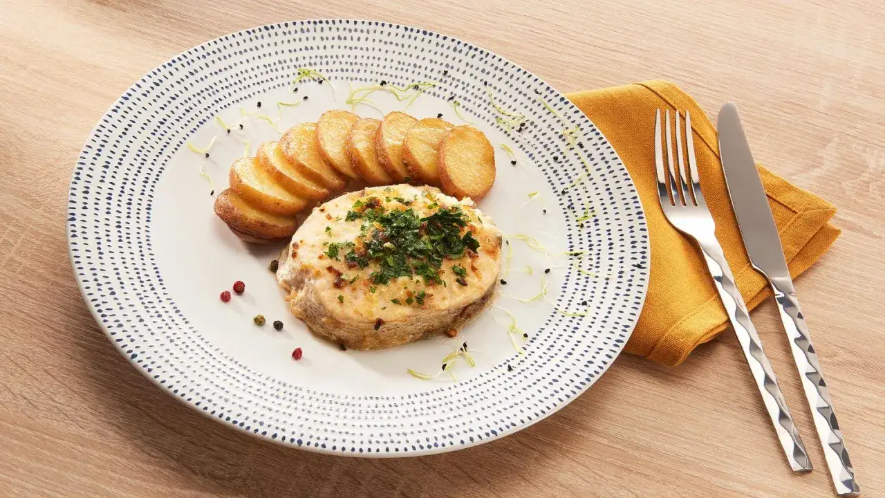 Merlu po&ecirc;l&eacute;, dor&eacute; et garni de persil, servi avec des rondelles de pommes de terre. Le temps cuisson merlu po&ecirc;le est parfait pour ce plat.