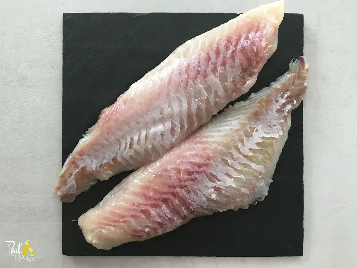 Deux filets de s&eacute;baste poisson, d'une chair blanche et ros&eacute;e, pr&ecirc;ts &agrave; &ecirc;tre cuisin&eacute;s sur une ardoise noire.