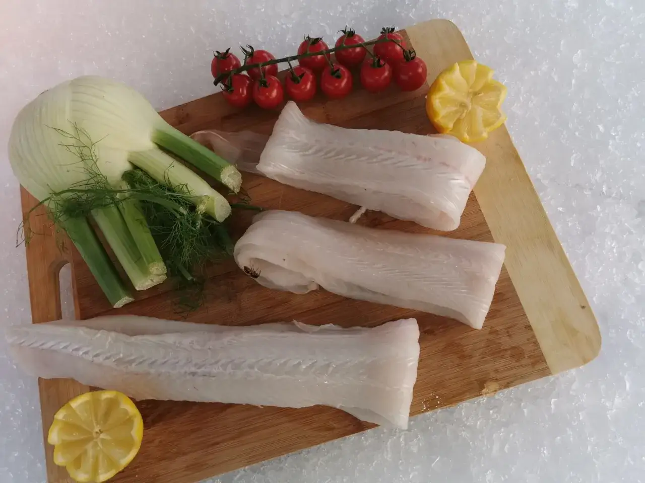 Trois filets de poisson sabre frais, pr&ecirc;ts &agrave; &ecirc;tre cuisin&eacute;s avec du fenouil, des tomates cerises et du citron.