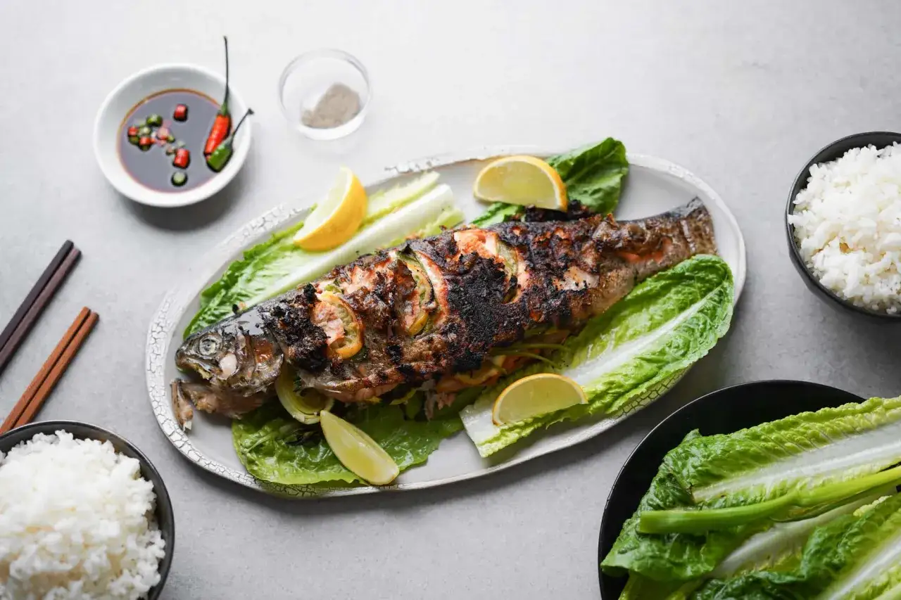 Poisson au barbecue grill&eacute;, garni de rondelles de citron et servi avec du riz et de la sauce piquante.