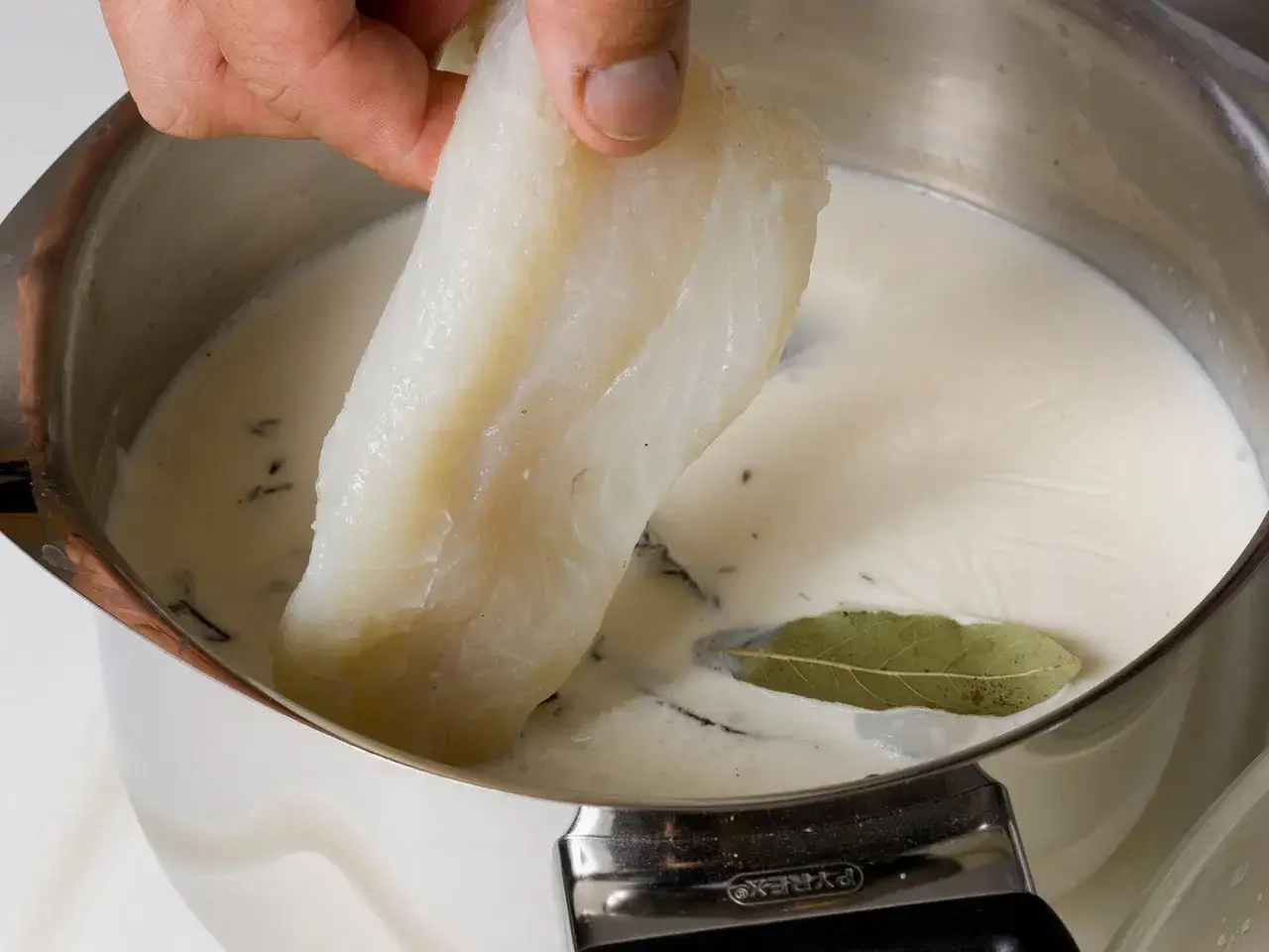 Un morceau de morue est plongé dans un liquide crémeux avec une feuille de laurier. Préparation d'une recette de morue.