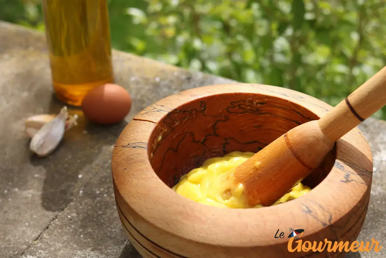 Pr&eacute;paration de la recette a&iuml;oli grand-m&egrave;re : mortier en bois, &oelig;uf, ail et huile d'olive pour une sauce cr&eacute;meuse.