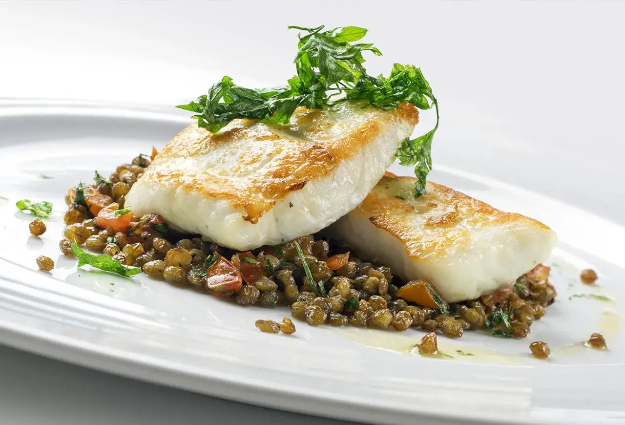 Deux pav&eacute;s de poisson colin po&ecirc;l&eacute;s, servis sur un lit de lentilles et de l&eacute;gumes, garni d'herbes fra&icirc;ches.