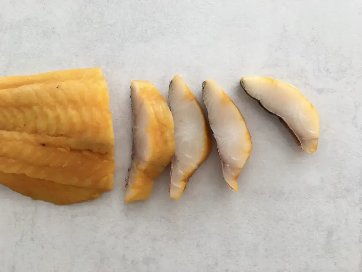 Un morceau de haddock poisson fumé, coupé en tranches, sur fond gris.