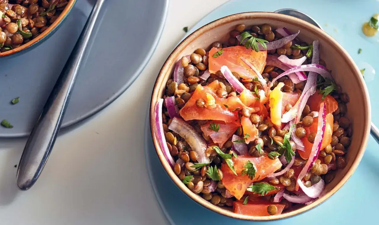 Salade de lentilles savoureuse avec des morceaux de saumon, des oignons rouges et du persil frais. Un plat léger et plein de saveurs.