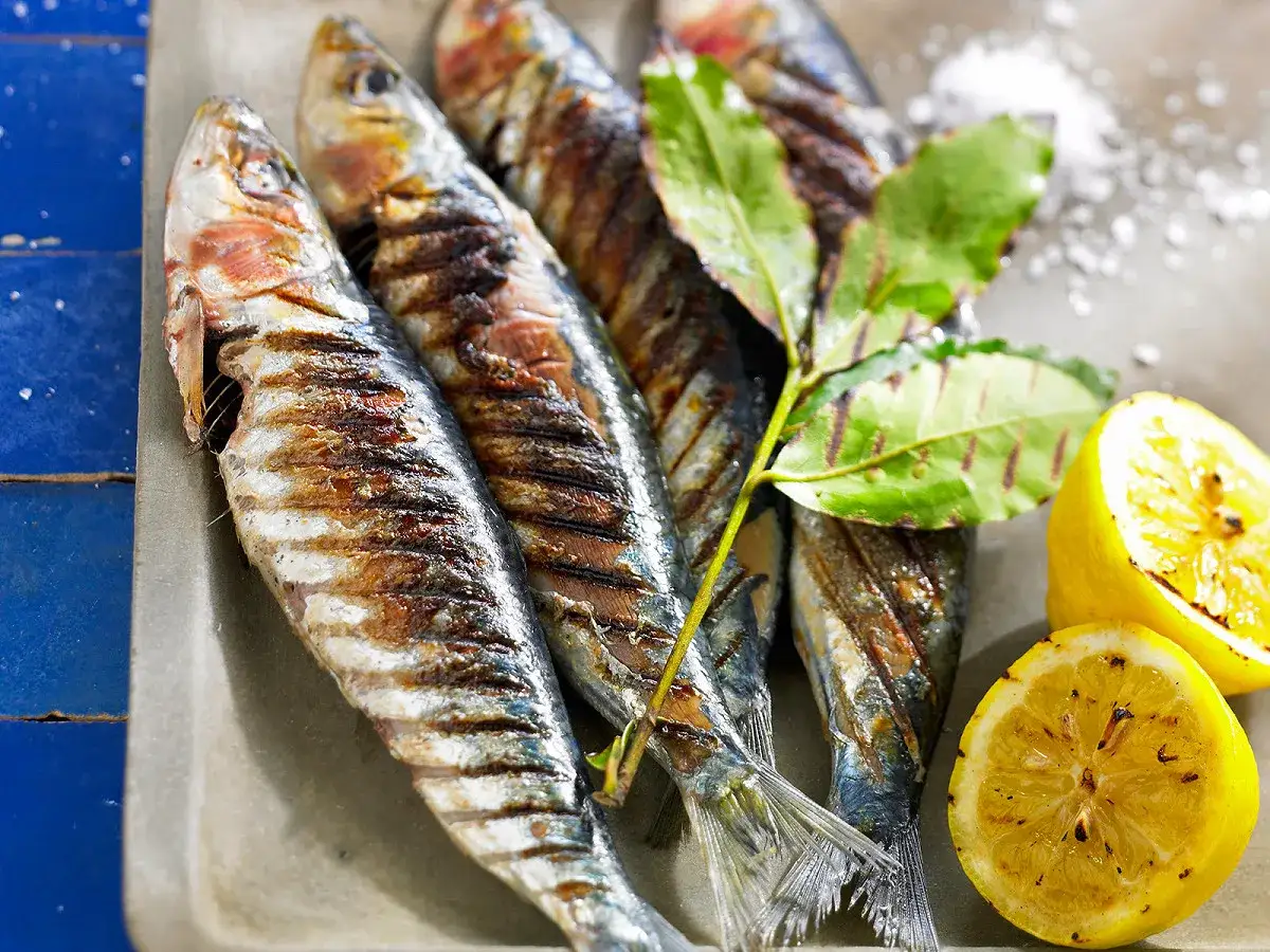 Sardines grill&eacute;es sur un plateau, garnies de feuilles vertes et de citrons r&ocirc;tis. Un d&eacute;lice de sardine barbecue.