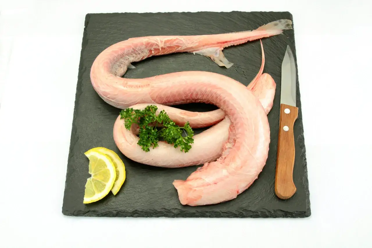 Saumonette de roussette crue, pr&ecirc;te &agrave; &ecirc;tre cuisin&eacute;e, avec des quartiers de citron, du persil et un couteau sur une planche d'ardoise.