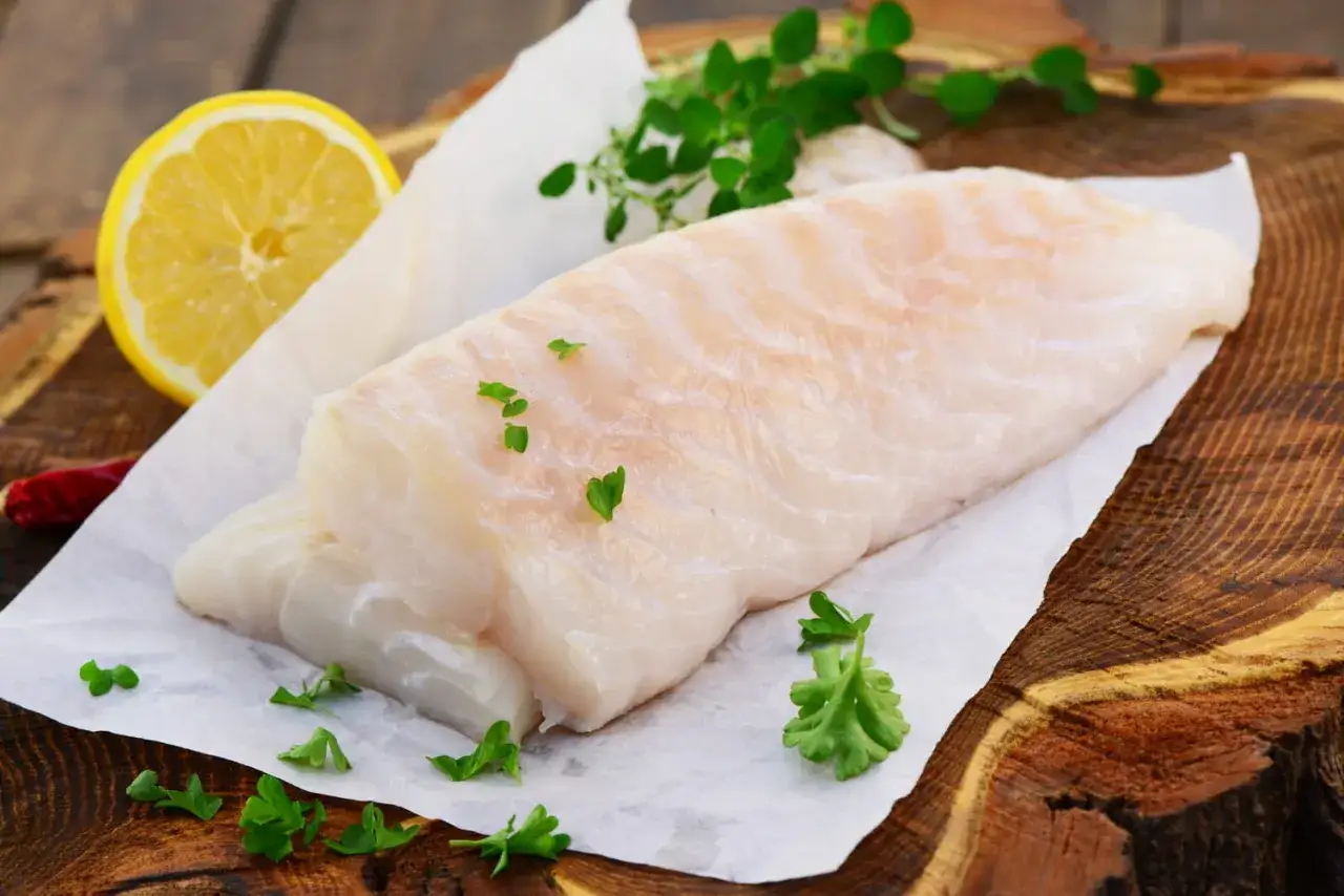Deux beaux filets de cabillaud poisson, pr&ecirc;ts &agrave; &ecirc;tre cuisin&eacute;s, avec du citron, des herbes et un piment sur une planche en bois.