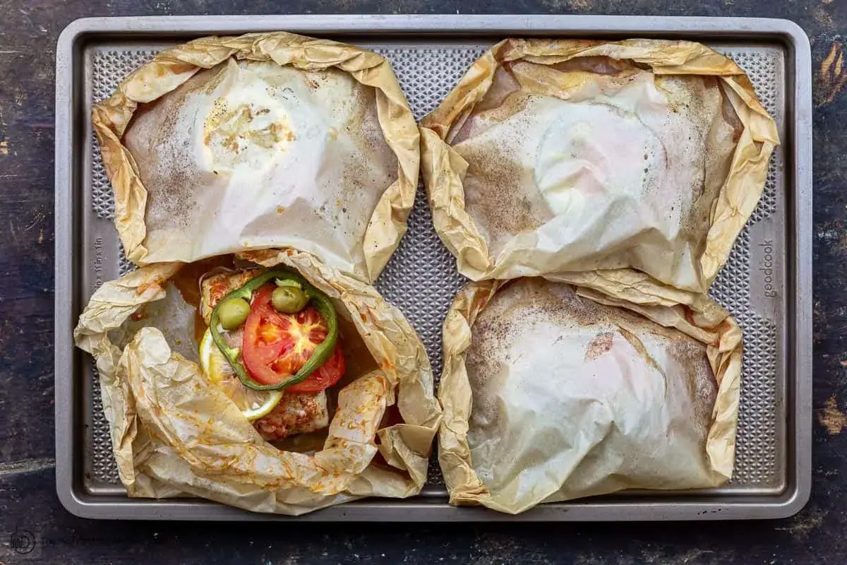 Quatre papillotes de poisson, dont une garnie de tomates, olives et citron. Un plat sain et savoureux d'églefin en papillote.