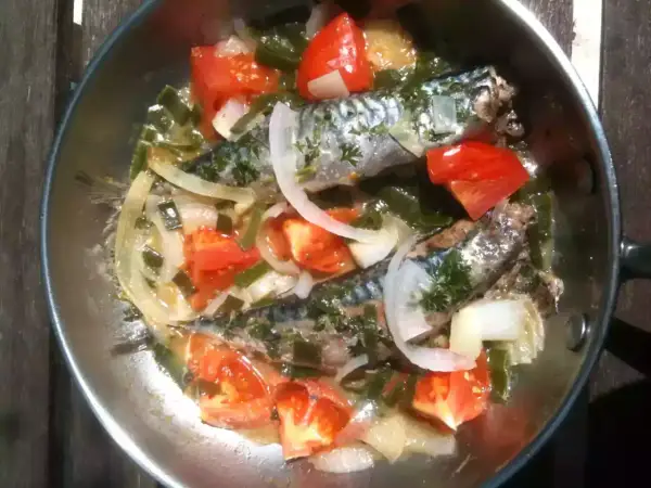 Deux maquereaux mijotent dans une poêle avec des tomates, des oignons et des herbes. Le temps de cuisson maquereau à la poêle est presque terminé.
