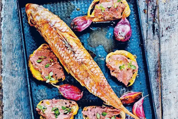 Un rouget barbet rôti sur un plateau avec des toasts tartinés de rillettes, des oignons rouges et des herbes.