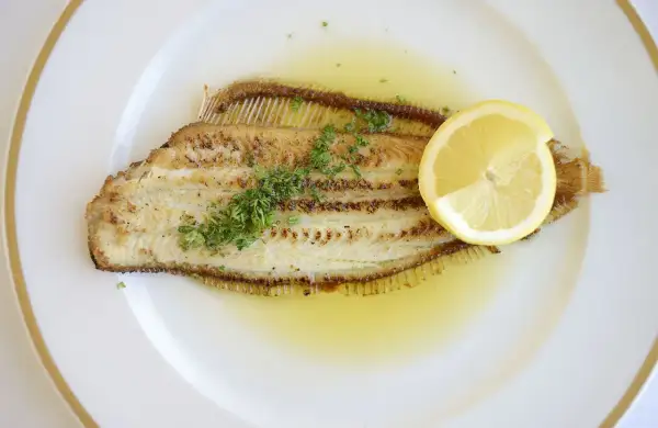 Un plat de sole meunière, un poisson délicatement poêlé, nappé d'une sauce au beurre et citron, garni de persil frais et d'une tranche de citron.