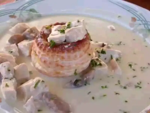 Un délicieux vol au vent aux crevettes, garni de morceaux de volaille et de persil frais, baignant dans une sauce crémeuse.