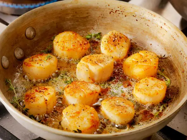 Poêlée de Saint-Jacques dorées, parsemées de poivre, dans du beurre mousseux avec du thym. Une recette coquille Saint-Jacques simple et savoureuse.