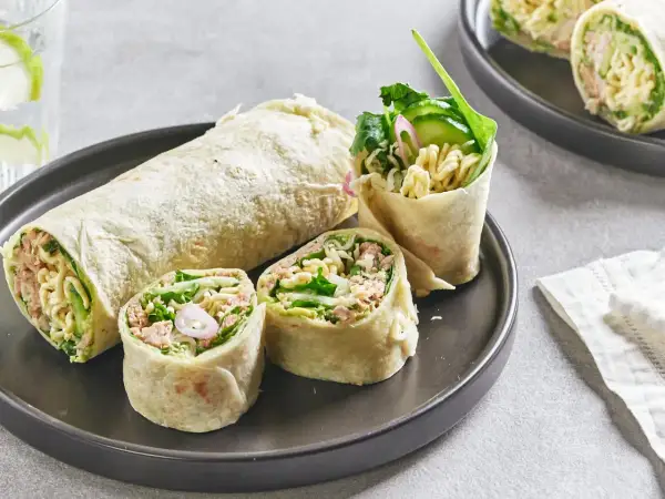 Wrap thon garni de nouilles, concombre et légumes verts, coupé en tronçons sur une assiette.