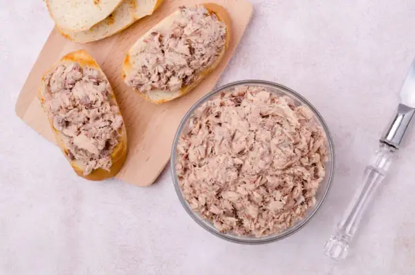 Tranches de pain garnies de rillettes de poisson, un bol rempli de rillettes de poisson et un couteau.