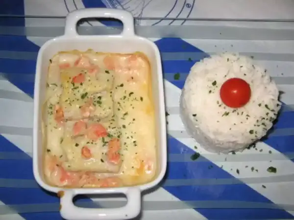 Poisson en sauce normande, parsemé de persil, servi avec une timbale de riz et une tomate cerise.