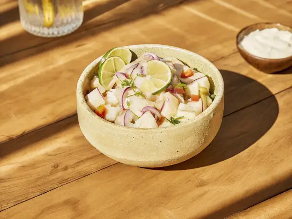 Un bol de ceviche frais, garni de rondelles de citron vert et d'oignon rouge. Une recette légère et savoureuse.