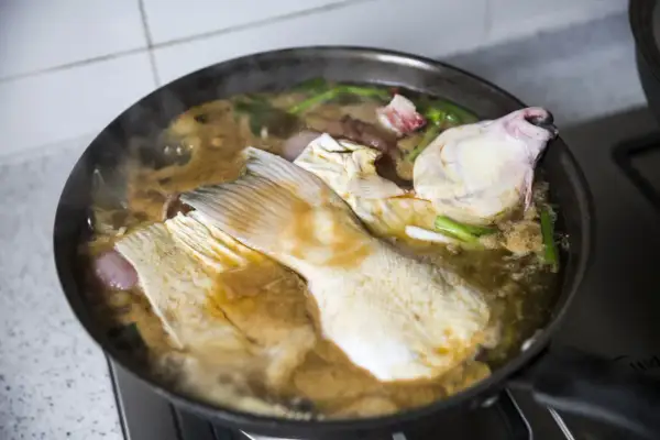 Morceaux de poisson mijotent dans une sauce matelote fumante avec des oignons et des herbes.