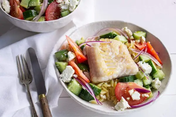 Salade de poisson méditerranéenne avec poisson blanc poêlé, concombre, tomate, oignon rouge et feta sur un lit de pâtes orzo.