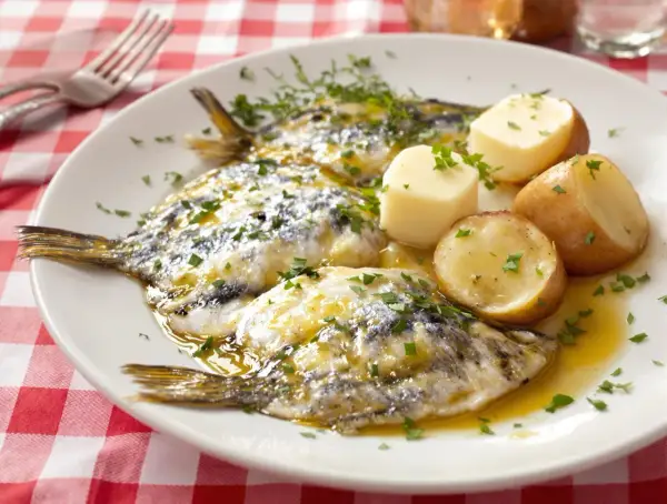 Assiette de harengs marinés avec pommes de terre et persil sur nappe à carreaux rouges.