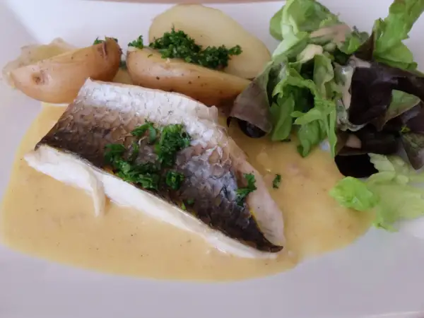 Filet de mulet poisson, servi avec des pommes de terre rôties, une salade verte et une sauce crémeuse.