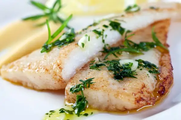 Deux filets de poisson maigre, dorés et garnis d'herbes fraîches, reposent sur une purée crémeuse. Un délice simple et savoureux.