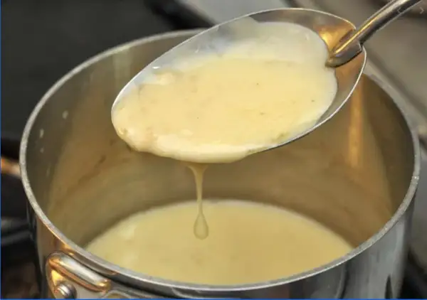 Une cuillère de sauce onctueuse, peut-être un beurre nantais, s'écoule dans une casserole.