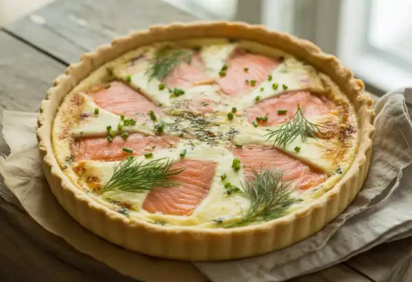 Quiche au saumon garnie d'aneth et de ciboulette, sur fond de bois.