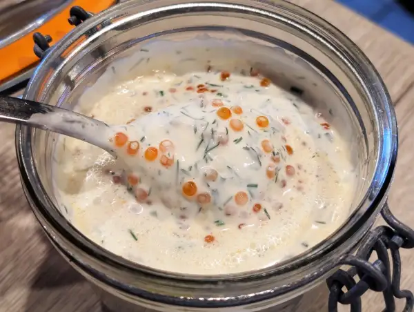 Une cuillère de sauce pour saumon crémeuse, parsemée d'aneth et de perles d'œufs de poisson, dans un bocal en verre.