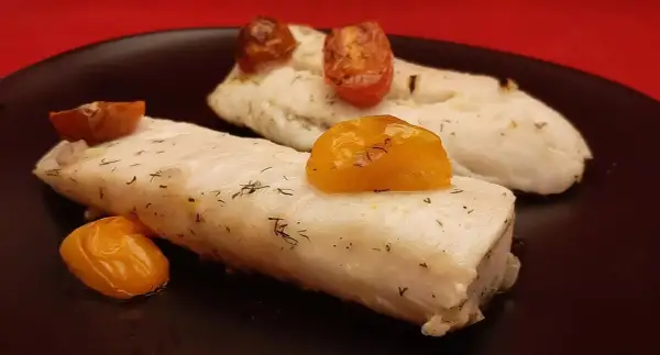 Deux filets de merlu au four, tendres et savoureux, ornés de tomates cerises rôties et d'aneth frais. Un délice simple et sain.