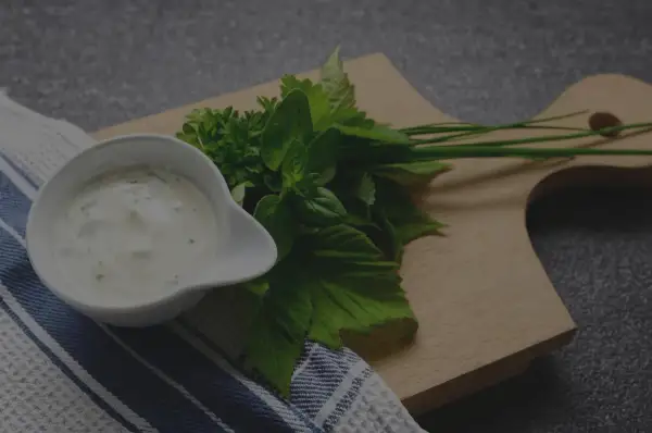 Un bol de sauce tartare crémeuse, garni d'herbes fraîches sur une planche en bois.