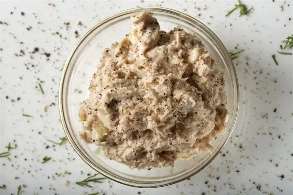 Un bol de rillettes de thon, assaisonnées de poivre noir et d'herbes, prêt à être dégusté.