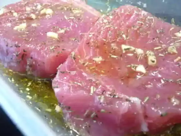 Deux beaux steaks de thon poisson marinés avec de l'ail et des herbes dans une huile dorée.