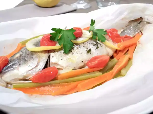 Dorade au four en papillote, garnie de tomates cerises, rondelles de citron, carottes et persil. Un plat sain et savoureux.