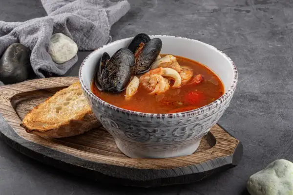 Bol de soupe de poisson aux moules et crevettes, servi avec une tranche de pain grillé et une touche de sauce rouille.