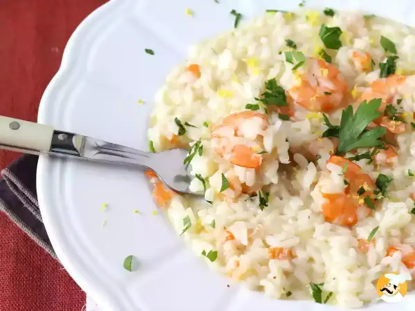 Un crémeux risotto fruits de mer, garni de crevettes roses, persil frais et zeste de citron. Une fourchette est plantée dans ce plat savoureux.