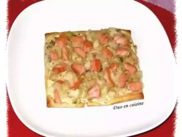 Tarte rectangulaire garnie de poireaux et de morceaux de saumon fumé, servie sur une assiette blanche.